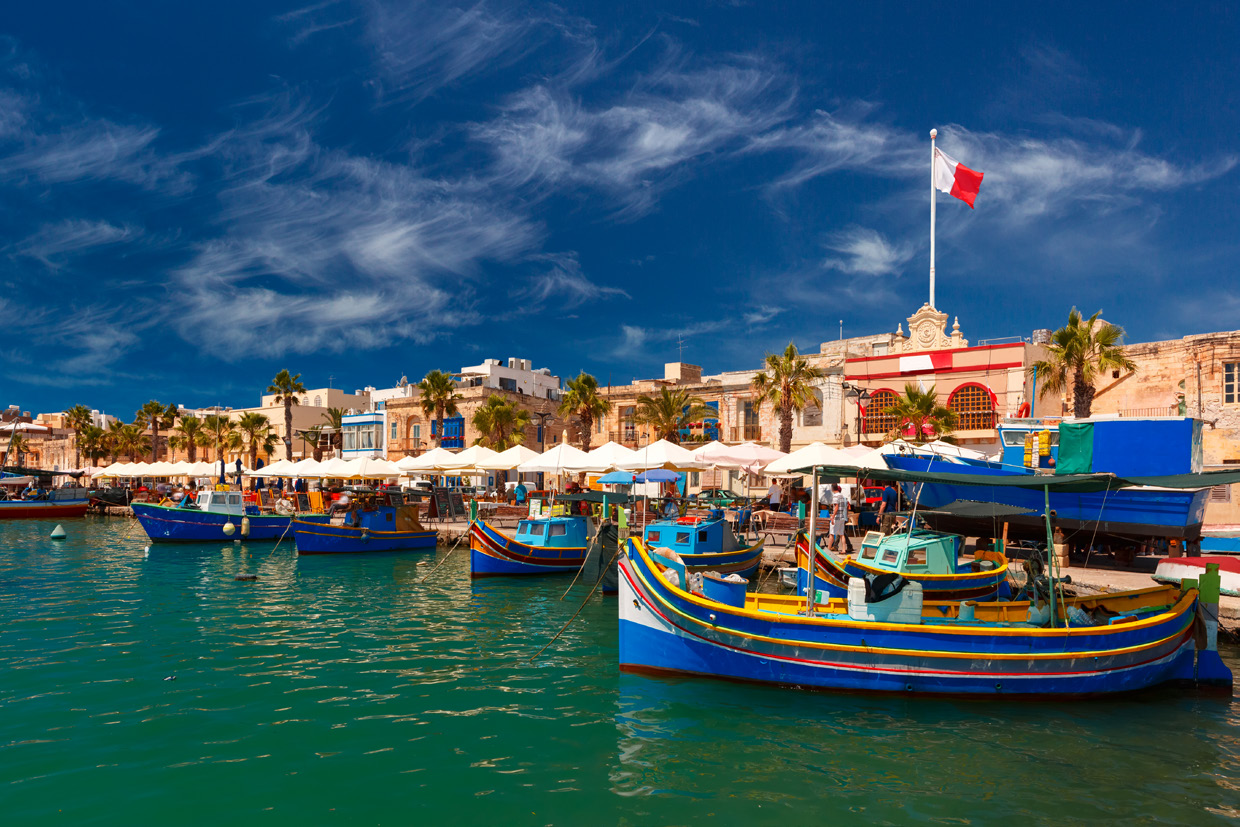 Traditional Maltese fishing harbor and national flag in Marsaxlokk